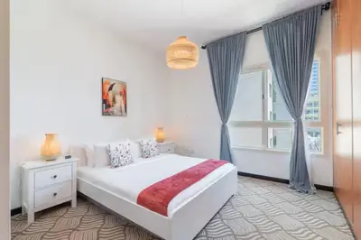a white bedroom with a large bed and a window at Vogue The Greens Al Alka near Mall of the Emirates, One Bedroom Apartment with Balcony and Vibrant community View, Access to all Amenities in Dubai