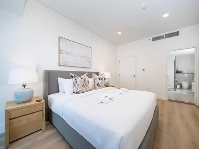 a white bedroom with a large bed and a night stand at Stunning 2-Bedroom Duplex in Dubai Marina in Dubai