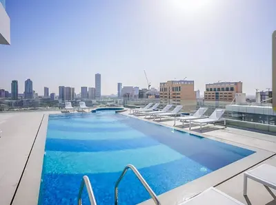 a swimming pool on the roof of a building with chairs at Cozy 1BR Apt in Bluebell Residences,JVC in Dubai