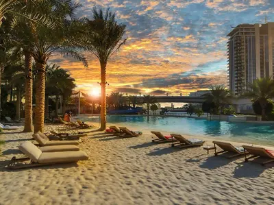 a beach with chaise lounges and palm trees at sunset at Luxury Apt and Private Beach with cooled sand in Dubai