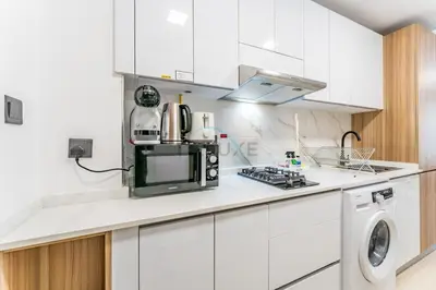 a kitchen with white cabinets and a microwave at Pool and Community View Studio with Balcony Near Park, Pantheon Elysee III, Jumeirah Village Circle by Deluxe Holiday Homes in Dubai
