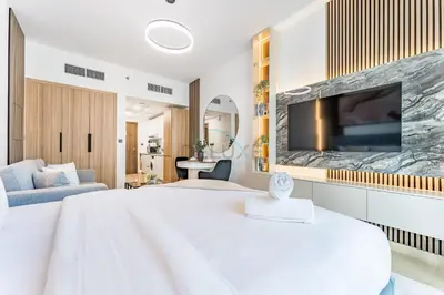 a white bedroom with a large tv on a wall at Pool and Community View Studio with Balcony Near Park, Pantheon Elysee III, Jumeirah Village Circle by Deluxe Holiday Homes in Dubai