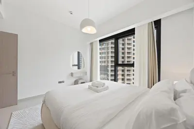 a white bedroom with a large white bed and a window at Act tower-1BR near burj khalifa in Dubai