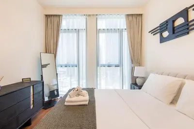 a bedroom with a white bed and a dresser and windows at Brand New Stylish 2 BR with Balcony in Dubai