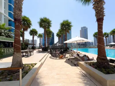 a resort pool with palm trees and chairs and tables at Luxury Canal-View Stay in Damac Privee in Dubai