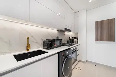 a white kitchen with a sink and a dishwasher at Chic Studio with Balcony and Gym at JVC in Dubai
