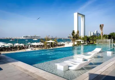 a swimming pool with white chairs and the ocean at La Vie Beachside Elegance in Dubai