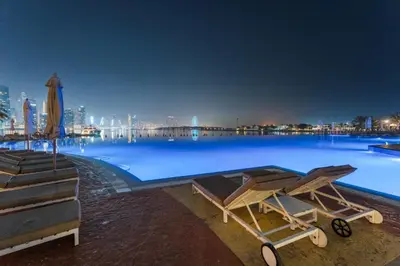 a large swimming pool with a city skyline at night at Resort Style 2BR Pool Access Private Beach in Dubai
