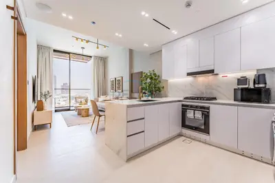 a kitchen with white cabinets and a living room at Community Views 1BR Next to Mall and Park, Binghatti Amber, Jumeirah Village Circle by Deluxe Holiday Homes in Dubai