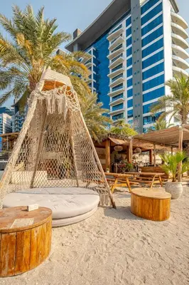 a hammock on the beach with palm trees and buildings at Modern 1BD, beautiful SeaView, Pool & Beach access in Dubai