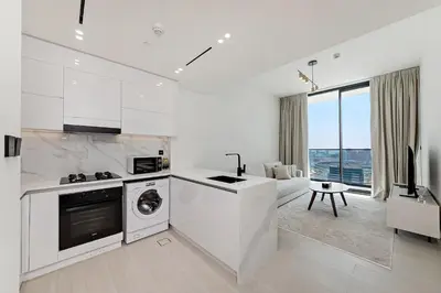 a white kitchen with a washing machine and a table at Cozy 1BR apartment in Binghatti Venus JVC in Dubai