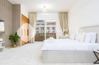 a white bedroom with a large bed and a window at Bloomfields Luxurious Stu in Mulberry 1 Emirates in Dubai