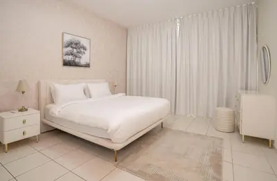 a white bedroom with a white bed and a window at Granduer 1 BR in Windsor Manor Canal Front Living With Burj Views in Dubai