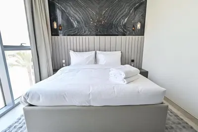 a bed with white sheets and pillows in a bedroom at Chic 2BR Heart of District One in Dubai