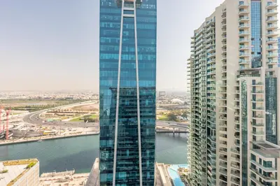 a tall glass building next to a body of water at 2BR Near Burj Khalifa & Business Bay Metro Station, Merano Tower, Business Bay in Dubai