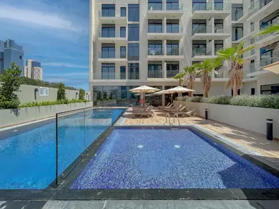 a swimming pool with chairs and umbrellas in front of a building at Luxurious Nature with 5 Star Amenities in JVC in Dubai