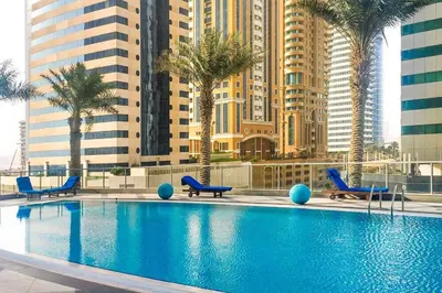 a swimming pool with chairs and palm trees and buildings at Vogue Marina Torch Tower near JBR Beach and Dubai Marina Mall, Two Bedroom Apartment with Balcony and City Skyline View, Access to all Amenities in Dubai