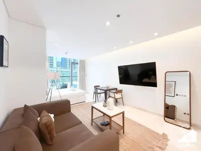 a living room with a brown couch and a mirror at Luxury at Sterling East Studio with Park Views in Dubai