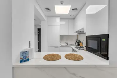 a white kitchen with two stools on a counter at Waves - Rustic Chic 1 BR Retreat in Vibrant JVC in Dubai