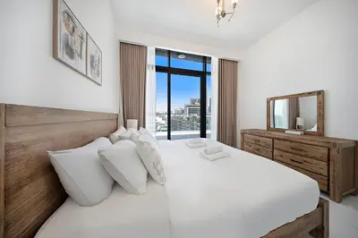 a white bedroom with a large bed and a mirror at Stylish 1BR with large Terrace JVC in Dubai