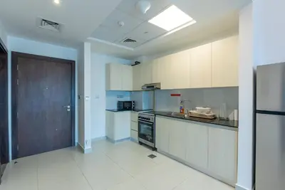 a kitchen with white cabinets and a brown door at 1 Bedroom in JVC in Dubai