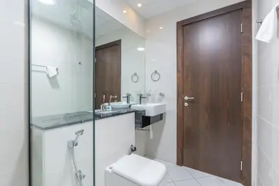 a bathroom with a toilet and two sinks and a wooden door at 1 Bedroom in JVC in Dubai