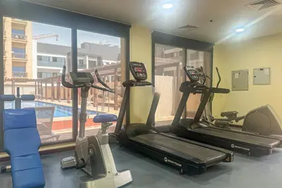 a gym with three exercise bikes and a swimming pool at Serene studio apartment with Burj Khalifa view in Jumairah Village Circle JVC in Dubai