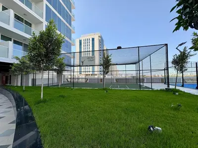 a tennis court in the grass next to a building at Dubai Studio Retreat Pool, Gym, Balcony & Queen Bed for Two in Dubai
