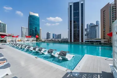 a large swimming pool with lounge chairs on a building at Vogue Downtown Mag318 near Burj Khalifa and Dubai Mall, Studio Apartment with Balcony, Canal and City View, Access to all Amenities in Sabkhah