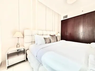 a white bedroom with a large white bed and wooden cabinets at Venduras- Chic 1BR Getaway near Burj Khalifa in Dubai