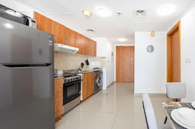 a kitchen with a stainless steel refrigerator and wooden cabinets at Chic 1BR Retreat with Lake Views & Modern Comforts in Dubai