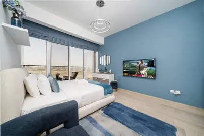 a bedroom with a white bed and a blue wall at Spacious JVC Studio Luxury Escape in Dubai
