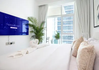 a white bedroom with a large bed and a tv at Luxury 2BR in Urban Oasis by Missoni on High Floor in Dubai