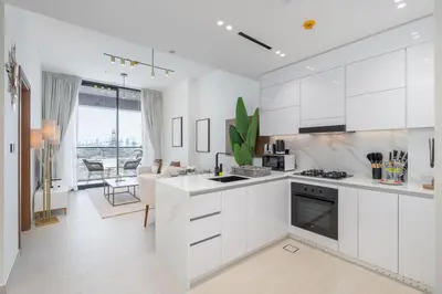 a kitchen with white cabinets and a living room at Golden Stays - Binghatti Onyx I Brand New 1BR I Modern and Fully Furnished in Dubai