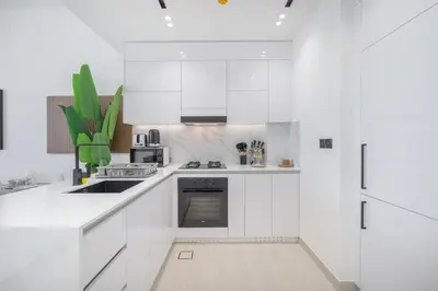 a white kitchen with white cabinets and a sink at Golden Stays - Binghatti Onyx I Brand New 1BR I Modern and Fully Furnished in Dubai