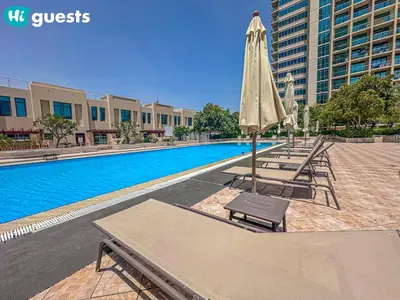 a pool with chairs and an umbrella next to a building at HiGuests - Luxe 2BR Overlooking Golf Course & Greenery in Dubai
