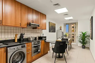 a kitchen with wooden cabinets and a table and chairs at Luxury 2BR with City Skyline Views Steps to JBR Beach & Marina Mall in Dubai
