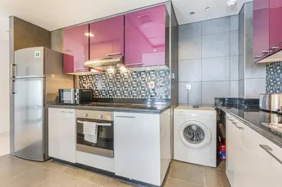 a kitchen with pink cabinets and a washer and dryer at 44th Floor Home at Cayan Tower with Panoramic Views in Dubai
