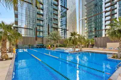 a large swimming pool with palm trees and tall buildings at Vogue Marina Gate near JBR Beach and Marina Mall, One Bedroom Apartment with Balcony and city skyline view, Access to all Amenities in Dubai