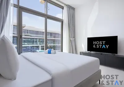 a white bedroom with a bed and a large window at Bright Studio in Loreto DAMAC Hills - Pet-Friendly in Dubai