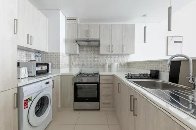 a kitchen with white cabinets and a washer and dryer at Stylish One-Bedroom Oasis - Prime Palm Location in Dubai