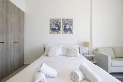 a white bedroom with a bed and a chair at Restay Homes - Chic Studio in JVC - Pool Views in Dubai