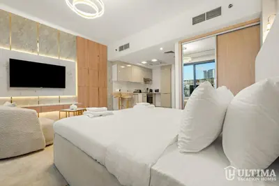 a bedroom with a large white bed and a living room at Lovely Studio in JVC with Summer Offer in Dubai