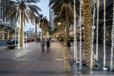 people walking down a street with palm trees and lights at Emaar Burj Crown - 1BR Sea View across from Burj Khalifa, walk to Dubai Mall in Dubai