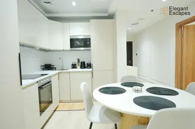 a white kitchen with a white table and chairs at Stylish 1B in Heart of Marina Near Attractions in Dubai