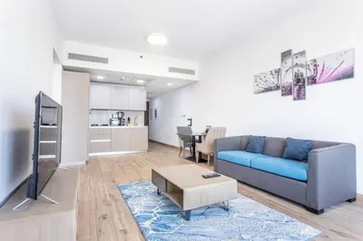 a living room with a blue couch and a kitchen at VacayLettings - 1 BHK - Near Jebel Ali Port- IKEA - Metro 20 Min - Al Furjan in Dubai