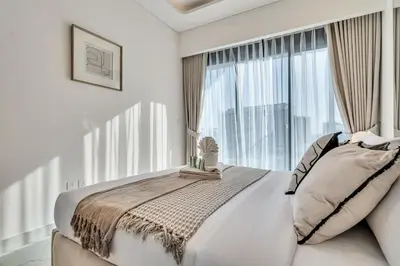 a white bedroom with a bed and a large window at Elegant 1-Bed with Pool, Gym, Parking and Balcony in Dubai