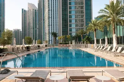 a swimming pool with chairs and palm trees and buildings at Spacious 4-Bedroom Apartment with Full Fountain and Burj Khalifa Views - 10 min Walk to Dubai Mall in Dubai