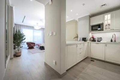 a kitchen with white cabinets and a living room at Stylish JVC 2BR Stay with Guest Room Rose Gold Accents in Dubai