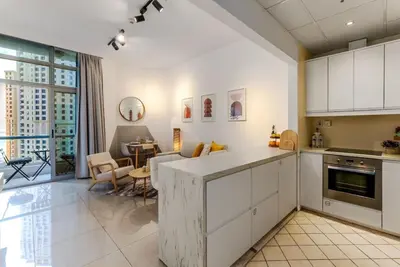 a kitchen with white cabinets and a living room at Marina Wharf 1 Bedroom with JBR Beach Views in Dubai